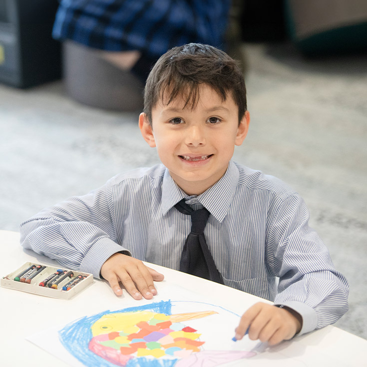 Student smiling at his desk with his artwork in the classroom at Our Lady of The Rosary Primary School Kellyville