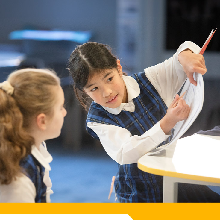 Student showing her classmate her workbook in the classroom at Our Lady of The Rosary Primary School Kellyville